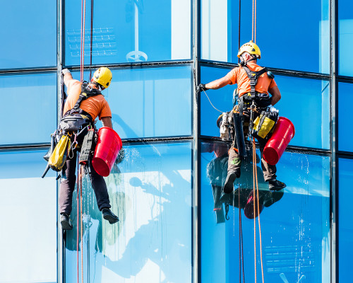 alpiniści myjący okna wysokiego budynku biurowego